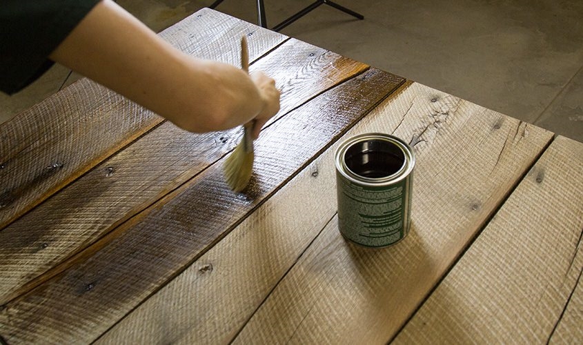 female using paintbrush to apply wood sealant